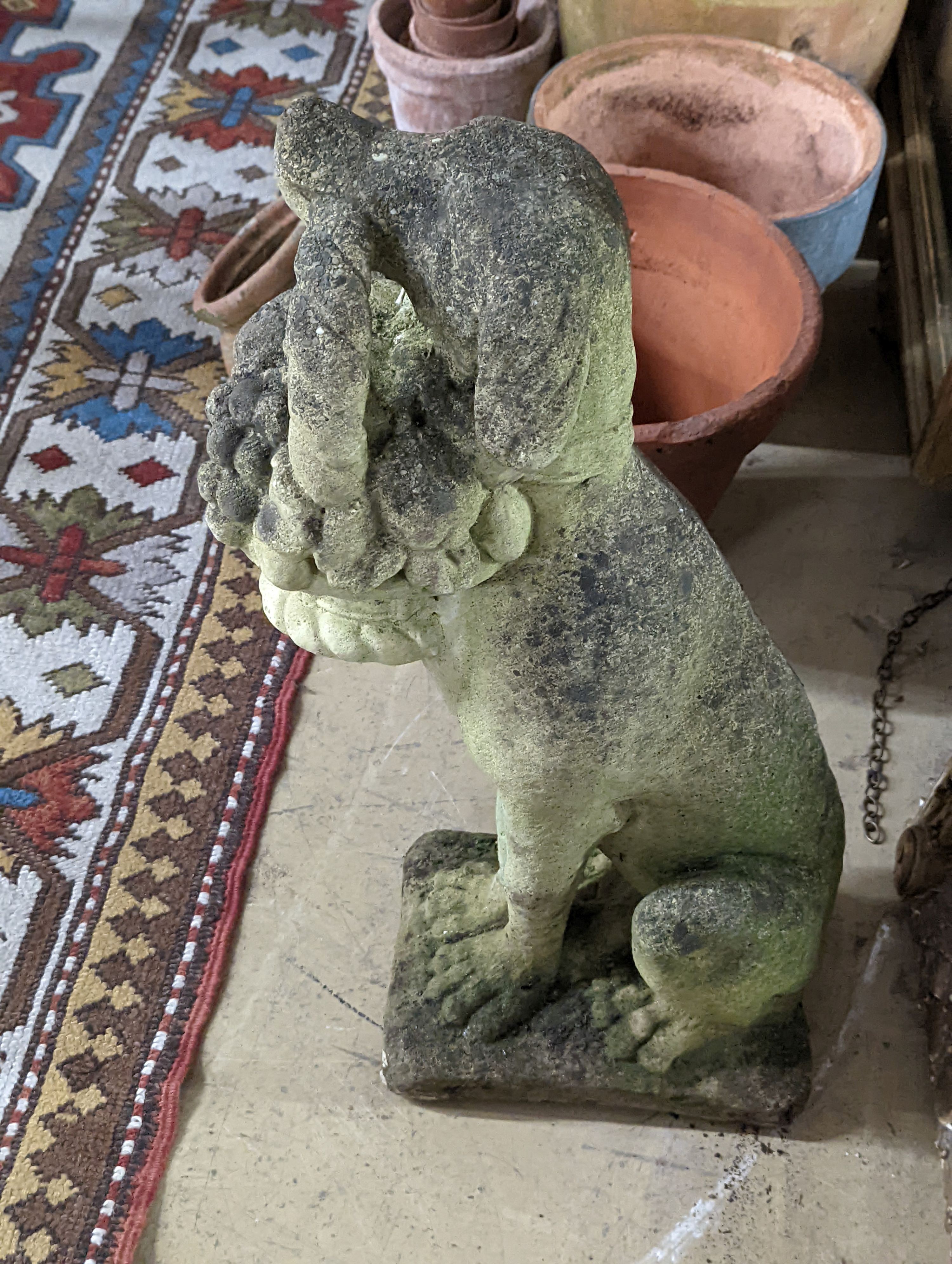 A reconstituted stone garden ornament of a seated hound, a basket of fruit in its mouth, height 60cm